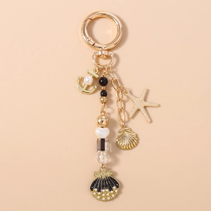 Close-up of golden nautical keychain with anchors, shells, and black pearls on beige backdrop