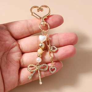 Dettaglio di un portachiavi a cuore dorato con perle bianche e ciondolo a fiocco di strass
