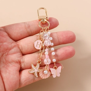Détail de breloques étoile de mer, papillon et perles roses sur porte-clés doré