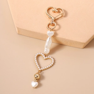 Detailed view of baroque pearl heart keychain with golden metal clasp on a beige stand