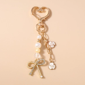 Dettaglio portachiavi con perle fiocco di strass e ciondoli a fiore in smalto bianco