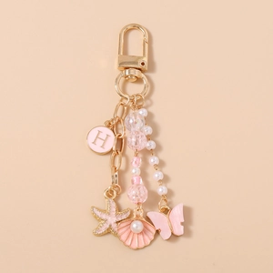 Détail du porte-clés doré avec lettre H rose, étoile de mer et breloques papillon