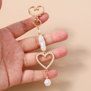 Detailed close-up of a vintage heart pearl keychain with golden baroque beads held by hand