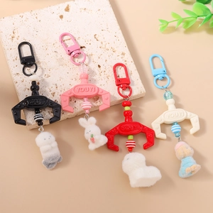 Plush animal claw machine keychains in black, pink, red, and white on a stone surface