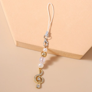 Detail of a sparkling musical note charm with rhinestones and white pearls on a gold chain