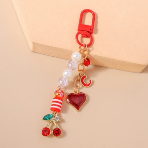 Detail view of a beaded keychain with cherry pendant and heart charm on a minimalist background