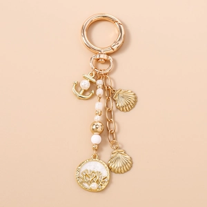 Détail d'un porte-clés nautique doré avec ancre, breloques coquillages et perles