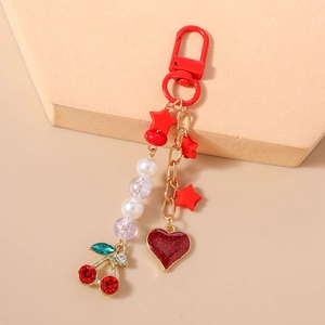 Detail of beaded keychain featuring red cherry and glitter heart charms on cream background