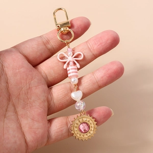 Vue détaillée du porte-clés en perles roses avec nœud et pendentif soleil doré en main