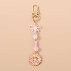Détail d'un porte-clés à nœud rose avec perles et pendentif soleil doré serti d'une gemme