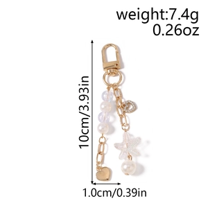 Detail view of gold keychain with faux pearls, starfish, and heart charms showing dimensions