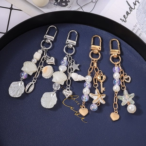 Marine style keychain charms with pearls, shells and starfish on dark blue tray