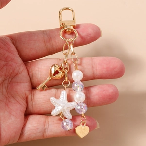 Detail of beaded keychain featuring heart key, starfish, and pearls held in hand