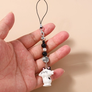 Detail view of a cat charm phone strap with white cartoon doll and beaded chain held in hand