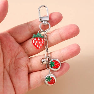 Detail of strawberry keychain with enamel charms and silver bell held by hand