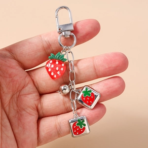 Detail of a strawberry metal keychain with 3D resin fruit and charms held by hand