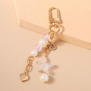 Close-up of golden keychain featuring beaded heart, iridescent starfish and white pearls