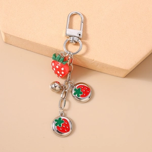 Close-up of strawberry keychain with silver lobster clasp, metal bell and charms