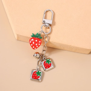 Detail view of strawberry keychain with silver metal charms and bell on neutral background