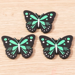 Detailed macro view of three butterfly charms with green patterns on a wooden surface