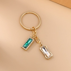 Golden keychain with emerald and clear square rhinestones on a warm beige background