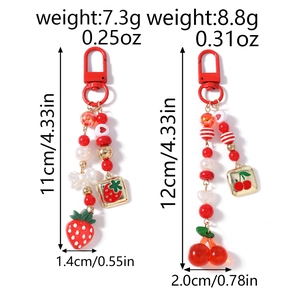 Close-up of beaded fruit keychains featuring red strawberry and cherry pendants with pearls