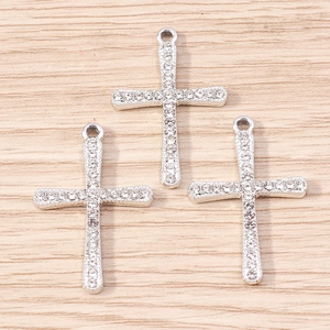 Three silver rhinestone cross pendants for DIY jewelry making on wooden background