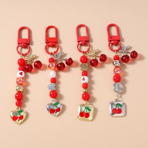 Detail of four beaded cherry themed keychains with red heart charms on a beige background