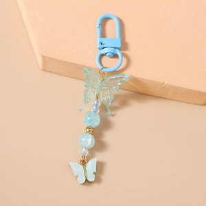 Macro detail of blue butterfly keychain with beaded charms and lobster clasp on beige base