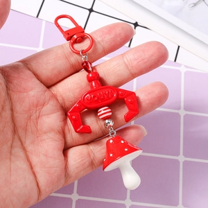 Close-up of a red mechanical claw keychain with a mushroom charm and striped bead