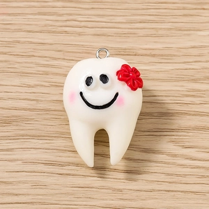 Dettaglio di un ciondolo a forma di dente in resina con fiore rosso e anello in metallo
