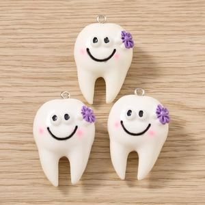 Tre simpatici ciondoli a forma di dente con fiori viola su sfondo in legno