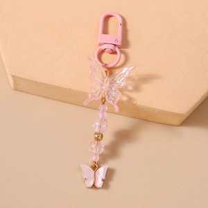 Detailed close-up of butterfly keychain with pink beaded chain on beige stone background