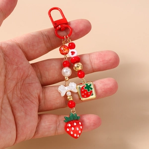 Detailed view of beaded strawberry keychain with red lobster clasp and white ribbon charm