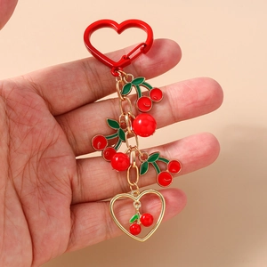 Detail of a red enamel cherry keychain with gold heart clasp and multi-layer bead accents