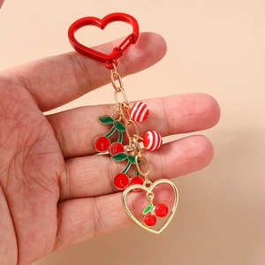 Detail of red cherry keychain featuring enamel charms and striped beads held by hand