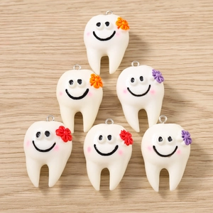 Dettaglio di ciondoli in resina a forma di dente con sorrisi e fiori per bigiotteria