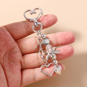 Détail d'un porte-clés coeur argenté avec nœud et perles tenu dans la main