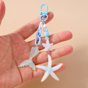 Detail showing hand holding an ocean theme keychain with fishtail and white starfish charms