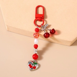Detail of beaded cherry keychain with red resin fruit and metallic heart pendant