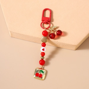 Detail shot of beaded cherry keychain with red beads and clear fruit charms on a beige stand