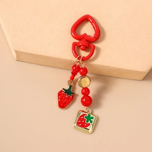 Close-up of strawberry keychain with heart clip, enamel charms and red beads on display