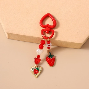 Detail of red strawberry keychain with heart-shaped beads and metal charm on stone base