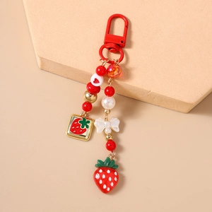 Detail view of red beaded strawberry keychain with golden accents and cream bow charm