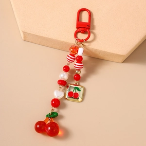 Detail of beaded cherry keychain with red carabiner and heart charm on a beige pedestal