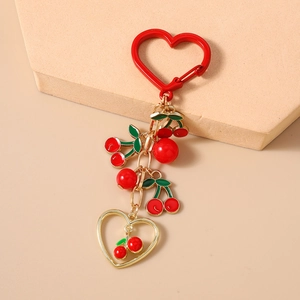 Detail of red cherry keychain with heart carabiner and golden hollow heart pendant charms