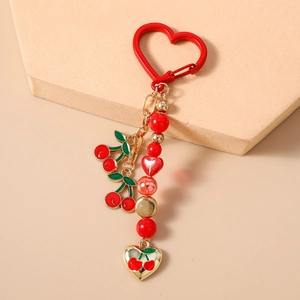 Detailed macro view of a red beaded cherry keychain with gold heart clasp and enamel charms