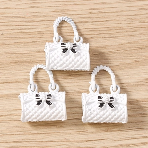 Macro detail of white quilted handbag charms with black bows and curved handles for DIY jewelry