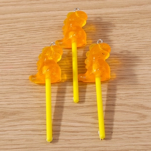 Vue détaillée de pendentifs sucettes dinosaures en résine orange avec paillettes
