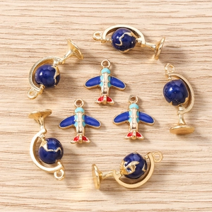 Gold-plated airplane and globe enamel charms for DIY jewelry making on wood background